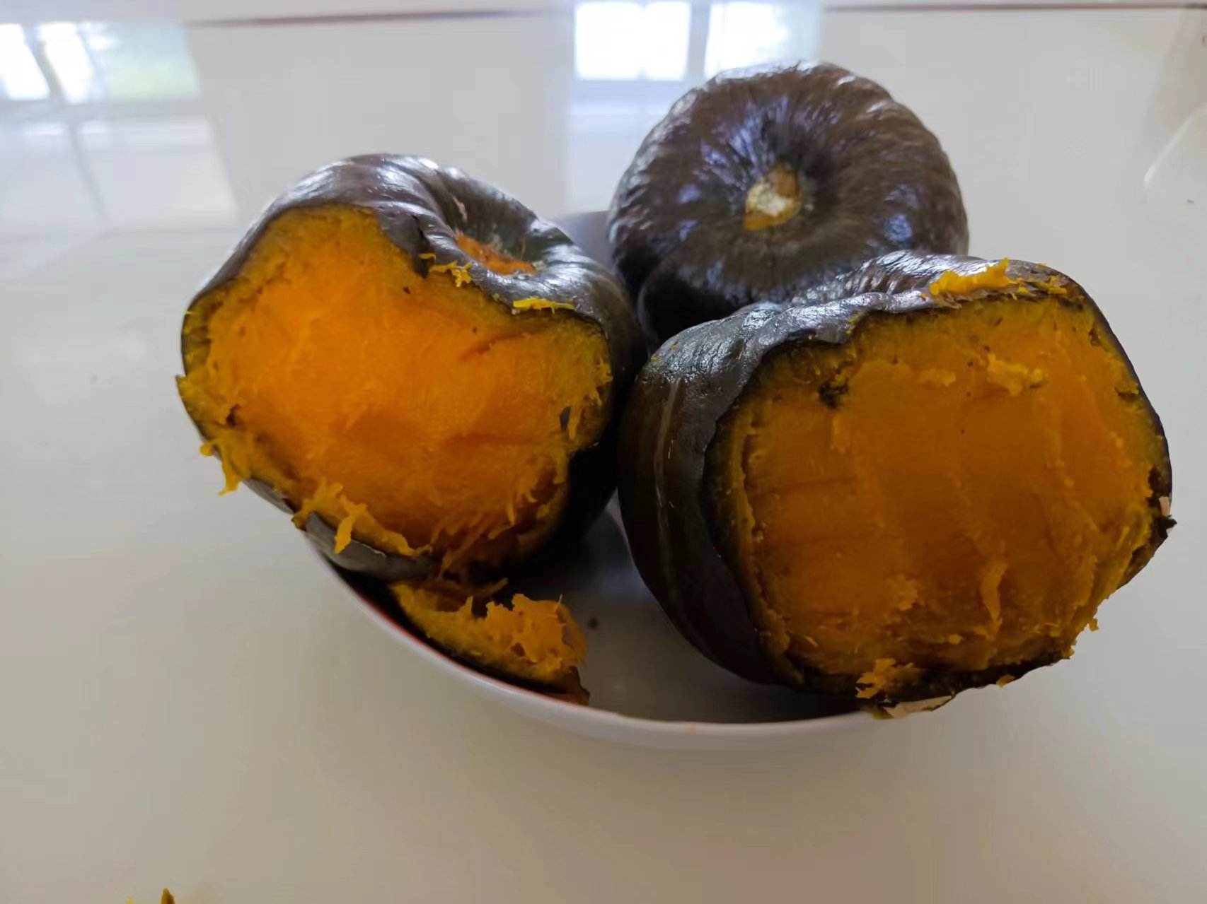 一个被纵向切开的贝贝南瓜,露出橙黄色的熟透果肉,表面微微起沙,左侧摆放着一小碟蜂蜜,右侧撒有切碎的核桃仁和杏仁片,展示多种食用搭配方式 蒸熟后切开的贝贝南瓜,果肉呈金黄色,质地细腻,旁边配有蜂蜜和坚果碎作为搭配建议