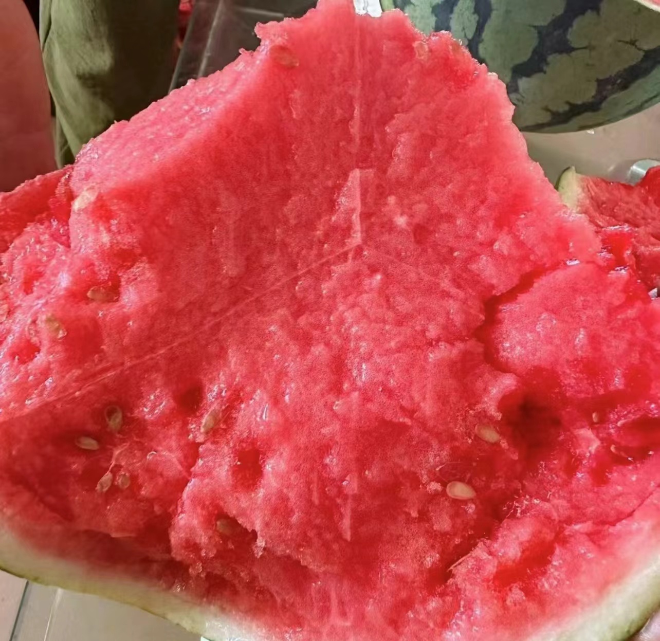 一颗被横向切开的卡其美都西瓜,露出鲜红色泽的果肉,中心部位颜色浓郁,汁水饱满,表面光滑无空心,黑色种子稀疏分布,周围摆放几片果肉展示其脆嫩质地 切开的卡其美都西瓜特写