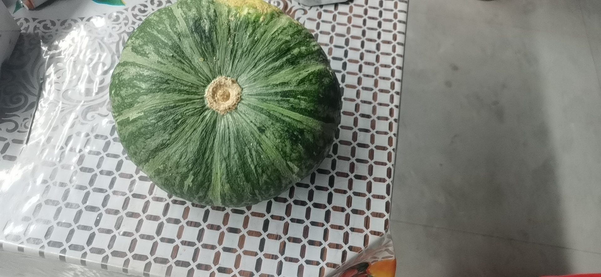 一个完整的板栗南瓜放置在木质砧板上,表皮呈均匀的橙黄色,略带浅绿色条纹,顶部带有绿色瓜蒂,光线柔和,背景为厨房环境 板栗南瓜整体外观特写