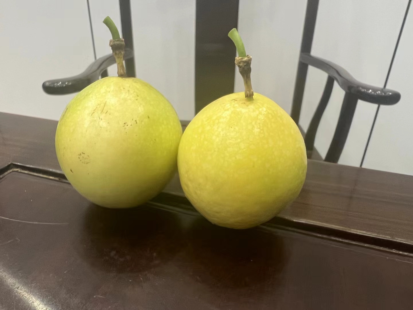 一颗成熟的黄金百香果,果皮光滑呈亮金色,表面无明显斑点,果实饱满圆润,背景为浅色木质桌面,旁边搭配一片绿叶和半切开的果肉,展示其内部透明籽粒和果汁丰富的状态 黄金百香果特写
