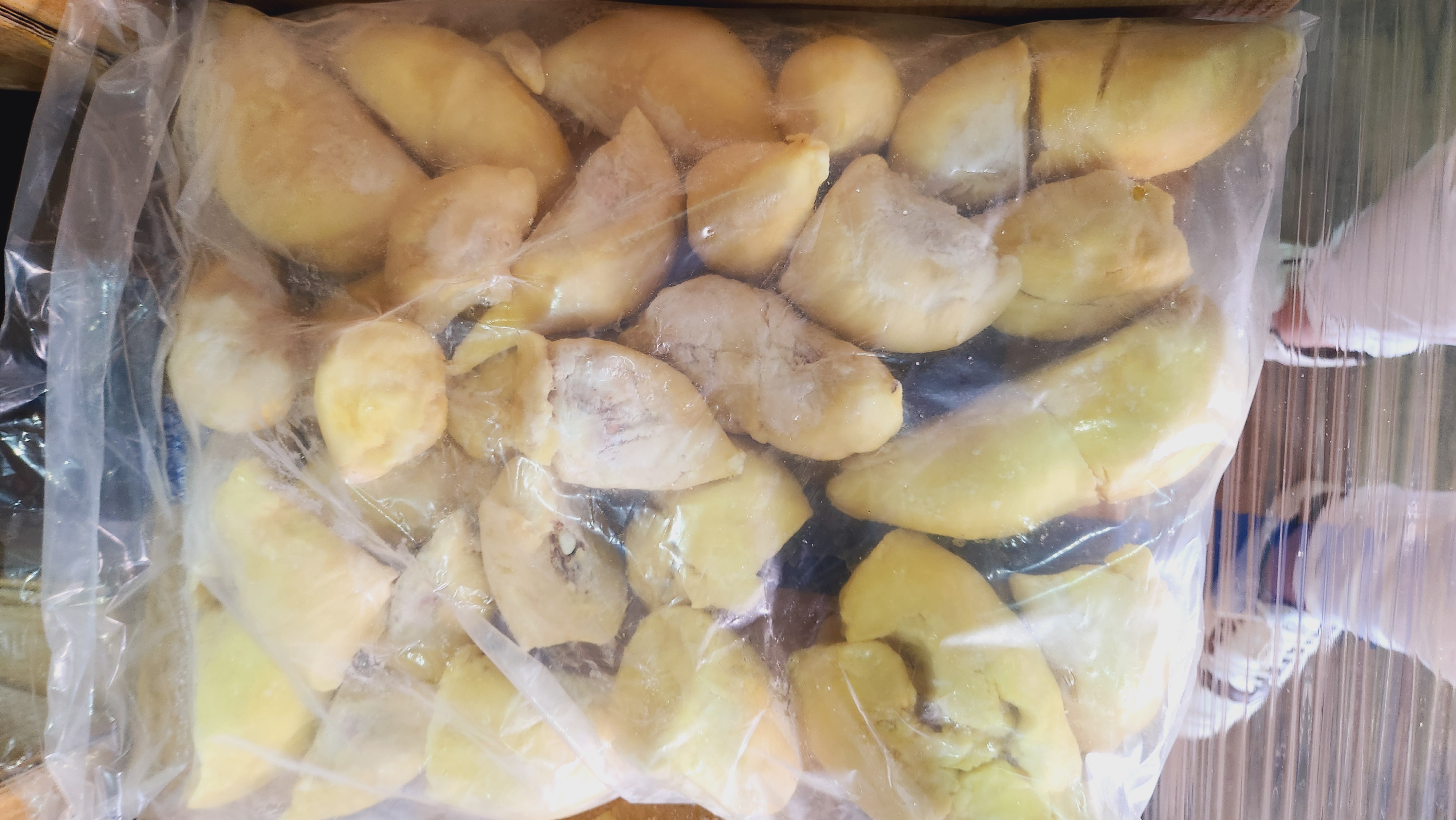 一只手戴着食品级透明手套,正从金枕头榴莲的深棕色外壳中取出一块完整的乳黄色果肉,果肉光滑饱满,旁边配有不锈钢小勺和白色瓷盘,背景干净整洁,展示果肉提取过程 金黄色果肉从榴莲壳中被手指完整取出,放在白色瓷盘上