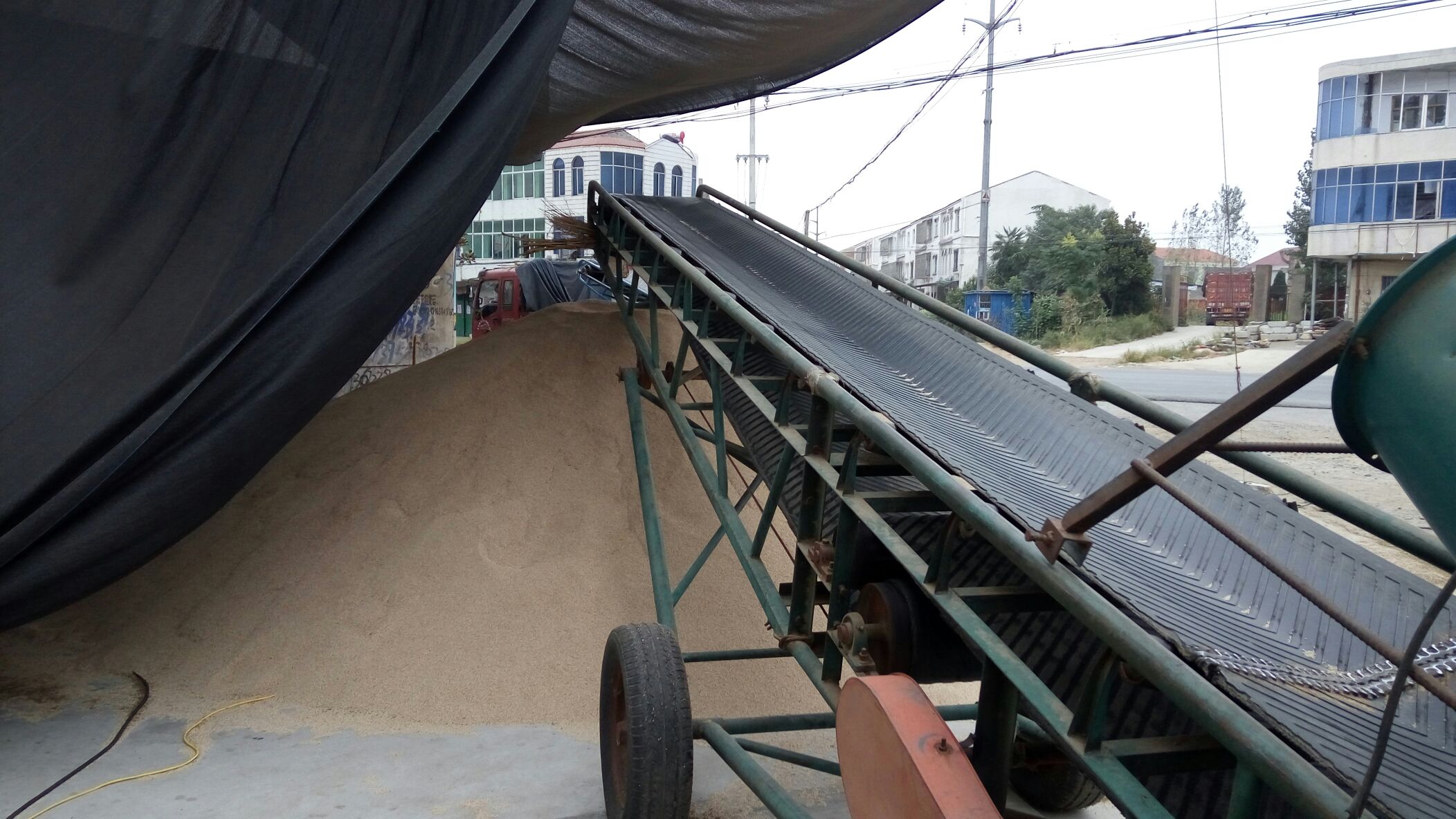 工厂车间内,一名身穿工作服的工人正在操作一台大型芝麻清理设备,机器由振动筛、风机和输送带组成,屏幕上显示着运行参数,传送带上流动着金黄色的芝麻籽,背景中有多个储料仓和管道系统 工人操作芝麻清理设备