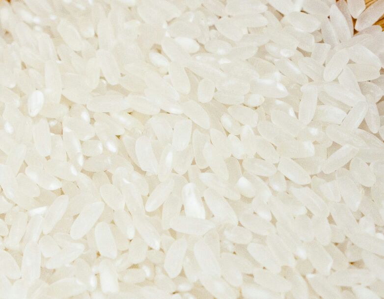 高清晰度微距摄影展示艳河长粒香大米单粒及群体状态,米粒细长透明,表面光滑有光泽,背景为木质餐桌与白色瓷碗,旁边放置稻穗样本,突出产品的天然质感与高端定位 艳河长粒香大米特写镜头