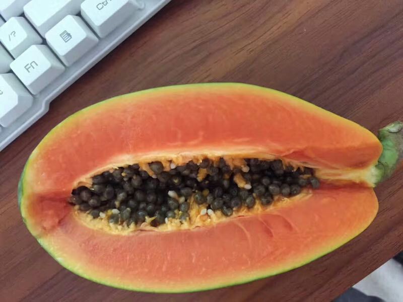 一个成熟的木瓜被横向切开,露出橙红色的果肉和黑色的籽粒,果肉质地细腻多汁,背景为浅色木质桌面,光线柔和自然 木瓜切开特写