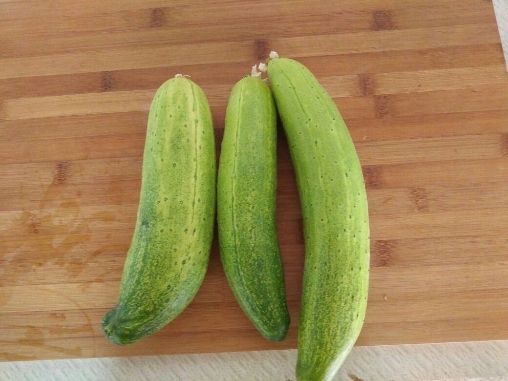 新鲜小黄瓜与辅料摆放图:展示主料和辅料的搭配,突出食材的新鲜度和色彩对比 新鲜翠绿的小黄瓜整齐摆放在木质案板上,旁边配有大蒜、小米辣和玻璃调味瓶