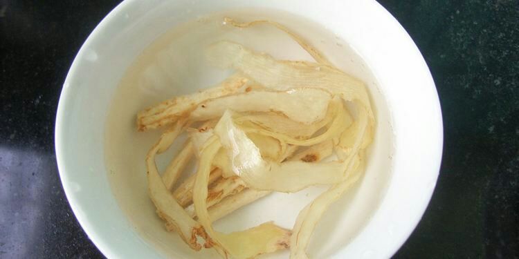 腐竹在透明玻璃碗中浸泡于清水中，旁边放有未泡发的干腐竹条作为对比