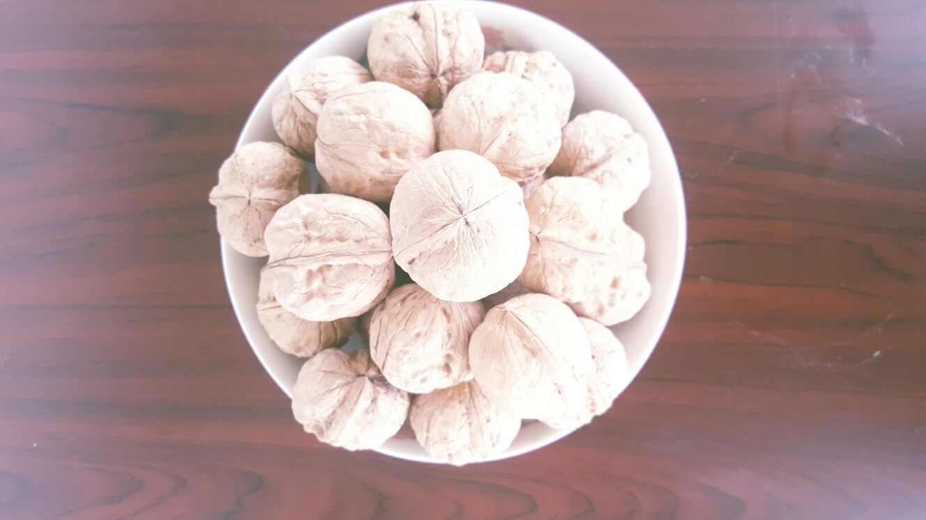 一个白色瓷碗中盛放着刚清洗晾干的新疆薄皮核桃,旁边是一小碟金黄色的蜂蜜与透明植物油混合液,一只手正用勺子将调料淋在核桃表面,核桃外壳呈现湿润反光状态 核桃调味过程特写
