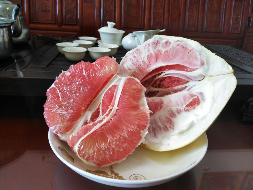 切开的泰国蜜柚特写，露出粉红色果肉，汁水欲滴，旁边配有勺子和玻璃杯榨好的柚子汁