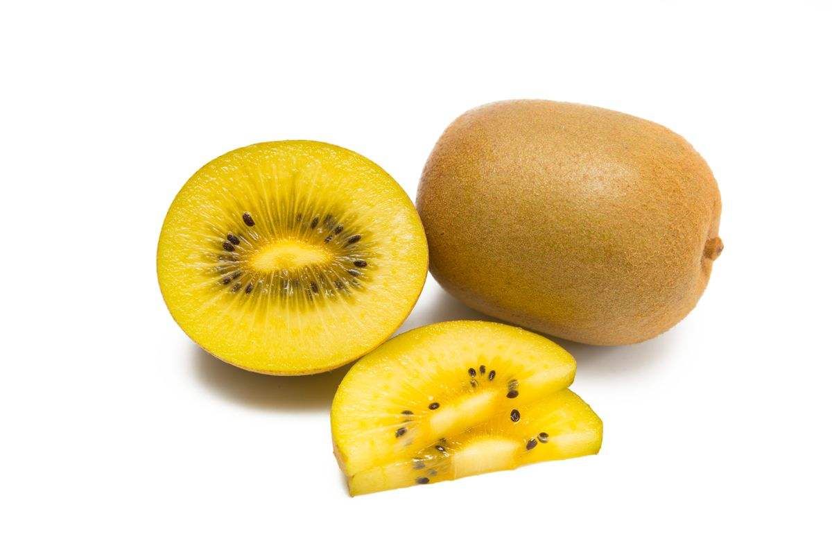 一颗成熟的黄心猕猴桃被横向切开,露出鲜艳的金黄色果肉,中心有放射状黑色小籽,果肉饱满多汁,边缘微微透明,旁边摆放一把银色小勺,背景为木质餐桌与绿叶装饰,突出新鲜与可食用性 黄心猕猴桃切开特写图