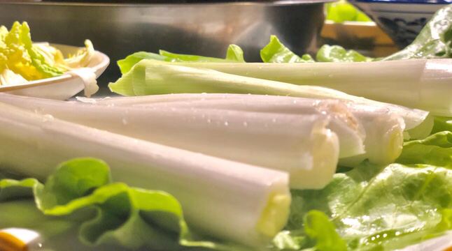 一张木质餐盘上摆放着数段切好的章丘大葱,呈放射状排列,中间放置一小碟深褐色甜面酱,旁边撒有少许香油滴落痕迹,整体风格自然质朴,突出食材本真之美 章丘大葱搭配酱料摆盘图