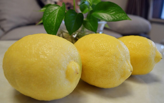 一颗金黄色、表皮光滑细腻的新鲜安岳柠檬,放置在木质砧板上,旁边有一把不锈钢水果刀,背景为自然光下的厨房环境,突出柠檬的新鲜与品质感 安岳柠檬特写