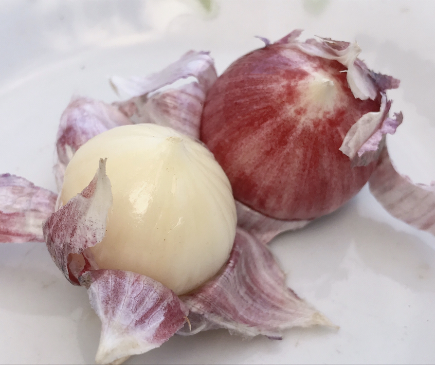 金黄色的烤独头蒜,外皮微裂,露出内部柔软的蒜肉,用叉子轻轻挑出半融化的蒜泥,背景为黑色石板,营造高级料理氛围 烤制后的独头蒜特写
