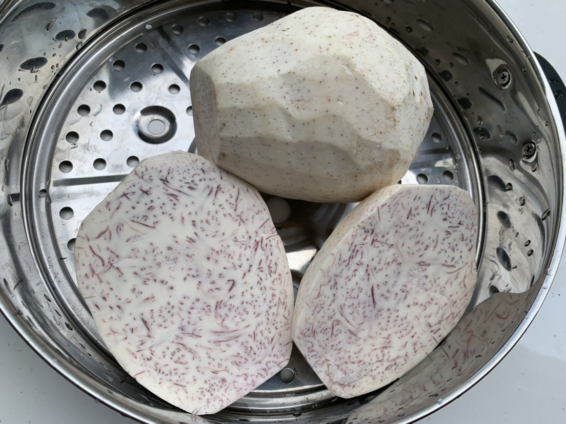 蒸熟的整颗香芋摆放在竹制蒸笼中，周围有几片绿色芋叶