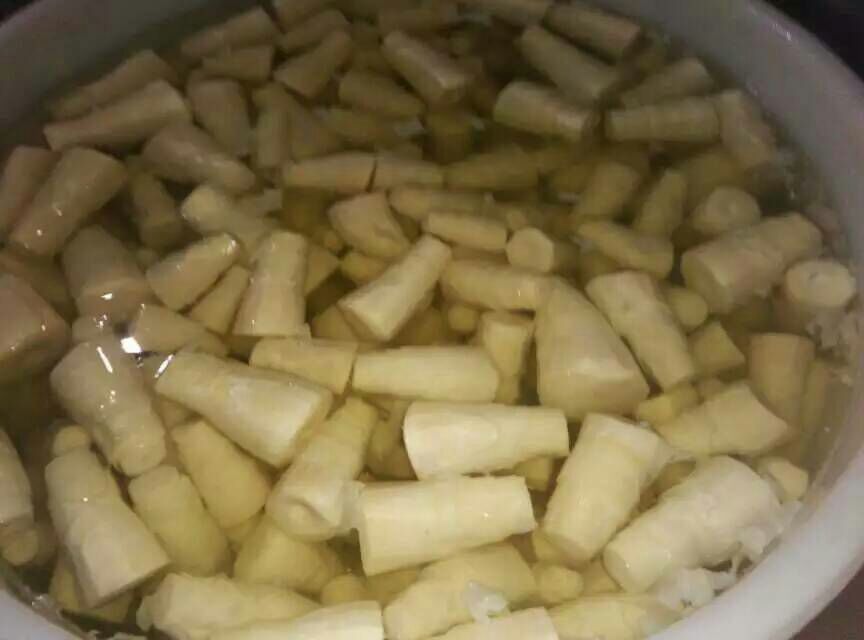 竹笋经沸水加碱焯烫3分钟后,迅速捞出投入盛有冰矿泉水的不锈钢盆中,笋片呈半透明浅黄色,表面水珠晶莹,背景为白色瓷砖操作台,体现'冷激定脆'关键步骤 新鲜竹笋焯水后浸入冰水的特写镜头