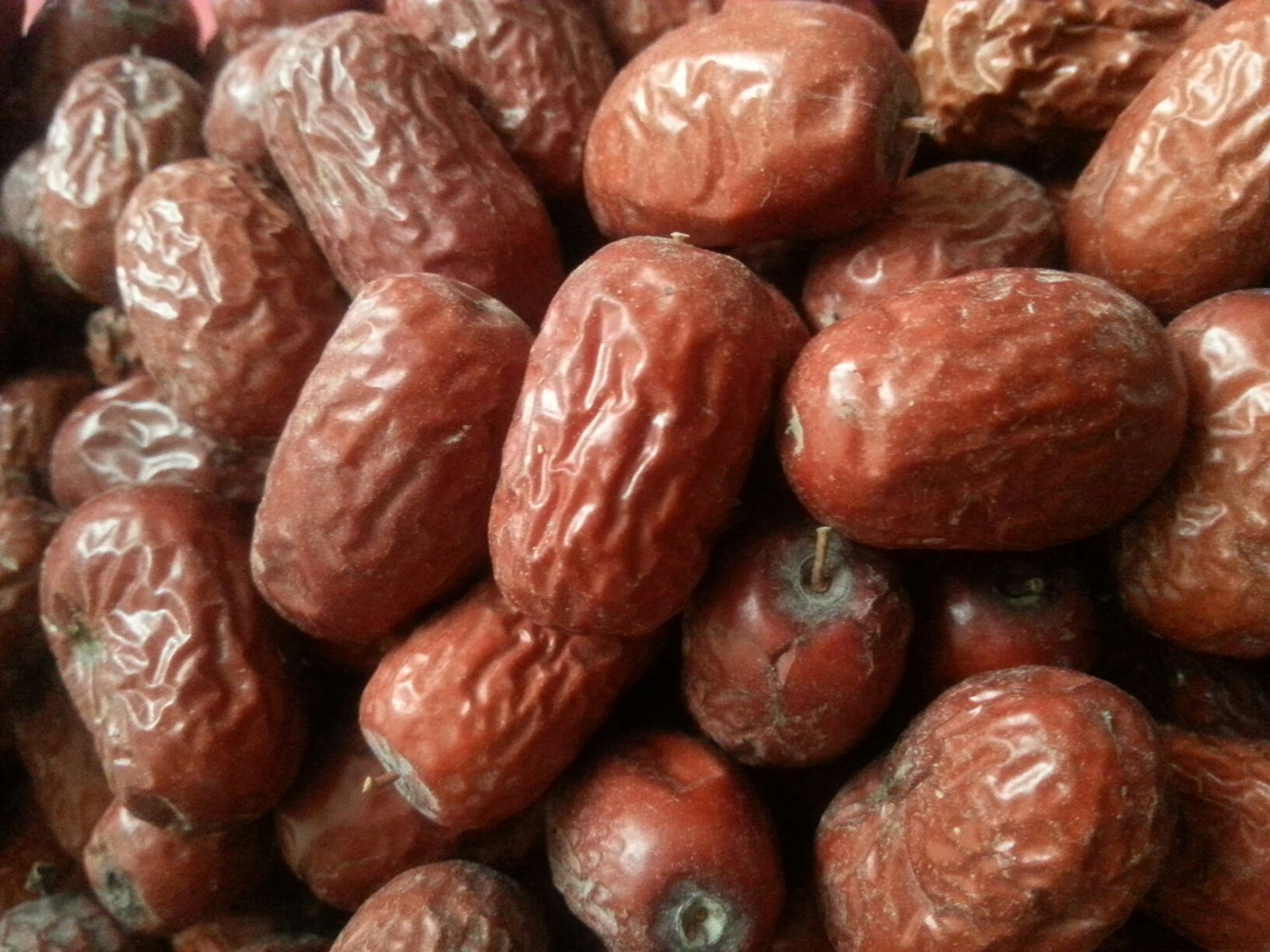 一颗成熟的擂枣特写镜头,果实呈深红亮泽,表面光滑无斑点,形状为长椭圆形,果体饱满,旁边放置标尺显示长度约4.5厘米,背景为新疆戈壁绿洲果园自然环境 擂枣特写