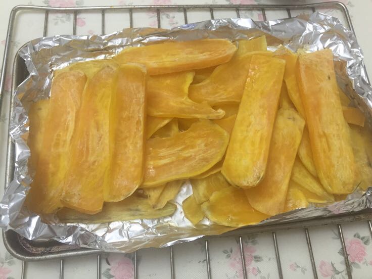 一张锡纸上放置两根完整带皮的烟薯,正准备送入家用烤箱,旁边有剪刀、手套和计时器,展示家庭自制烤烟薯的操作流程 家庭厨房中用锡纸包裹烟薯进行烤制的过程图