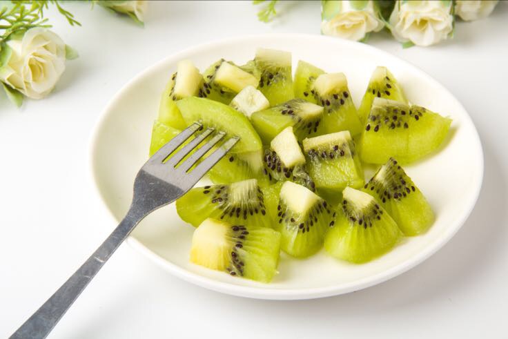 新鲜海沃德猕猴桃洗净后放在白色瓷盘上，旁边摆放一把银色小巧的水果削皮刀，背景为木质餐桌