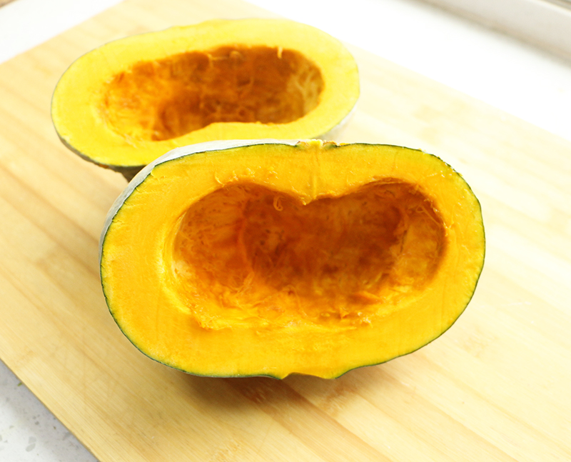 一个完整的板栗南瓜放置在木质砧板上,表皮呈深橘黄色,带有浅色纵向条纹,表面光滑无破损,旁边放有一把不锈钢厨刀,背景为自然光线下的厨房台面 板栗南瓜整体外观特写