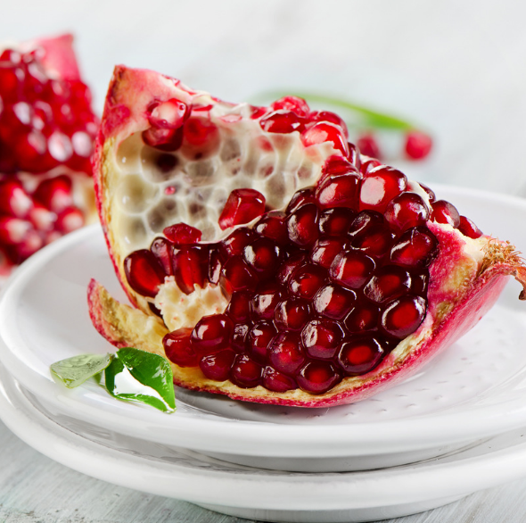 营养师现场演示：手持荥阳软籽石榴果实，掰开后用不锈钢小勺舀出完整特大籽粒，置于白色瓷盘中，旁边摆放橄榄油瓶、混合坚果和绿叶蔬菜，体现科学搭配场景