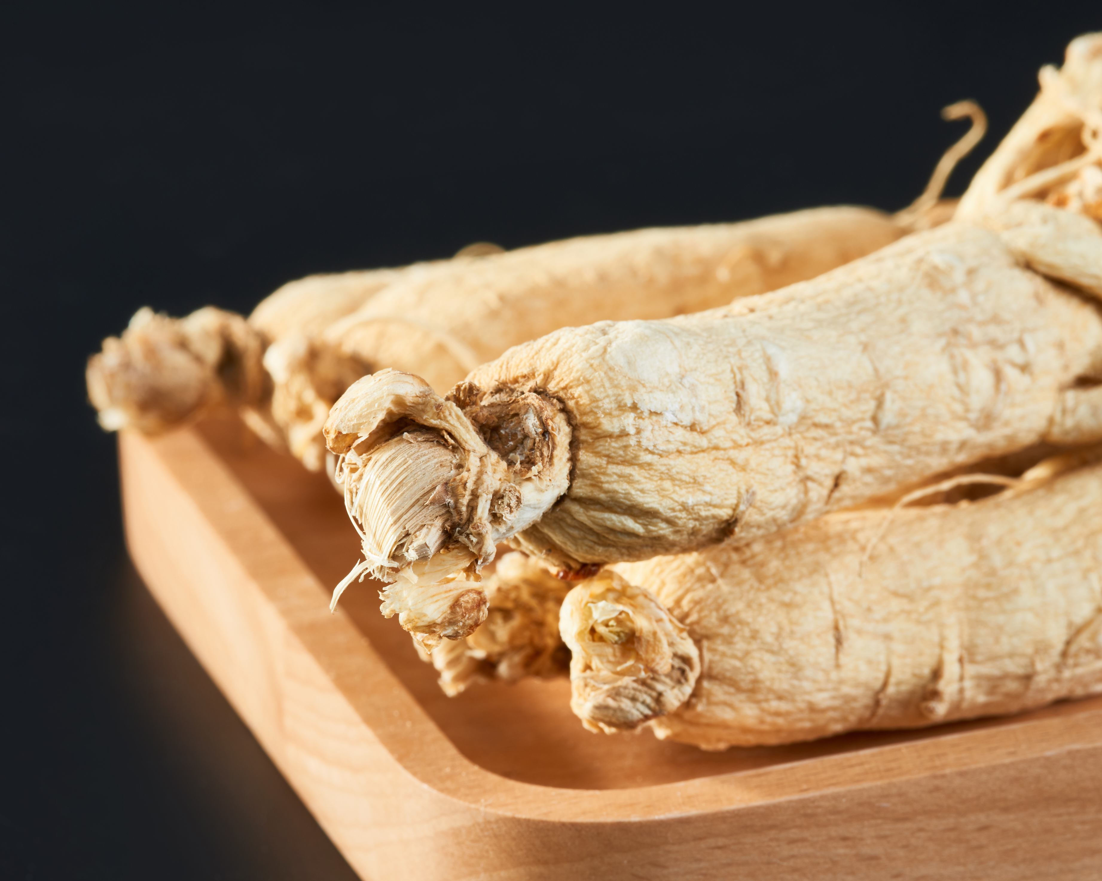 两张并列摆放的照片,左侧为一对完整的干海马,呈弯曲状,灰黄色,表面纹理清晰;右侧为数片薄切的生晒参,呈淡黄色,边缘整齐,带有自然参纹。背景为浅木色案板,旁边配有红枣、枸杞和姜片 海马与生晒参的原材料摆放示意图