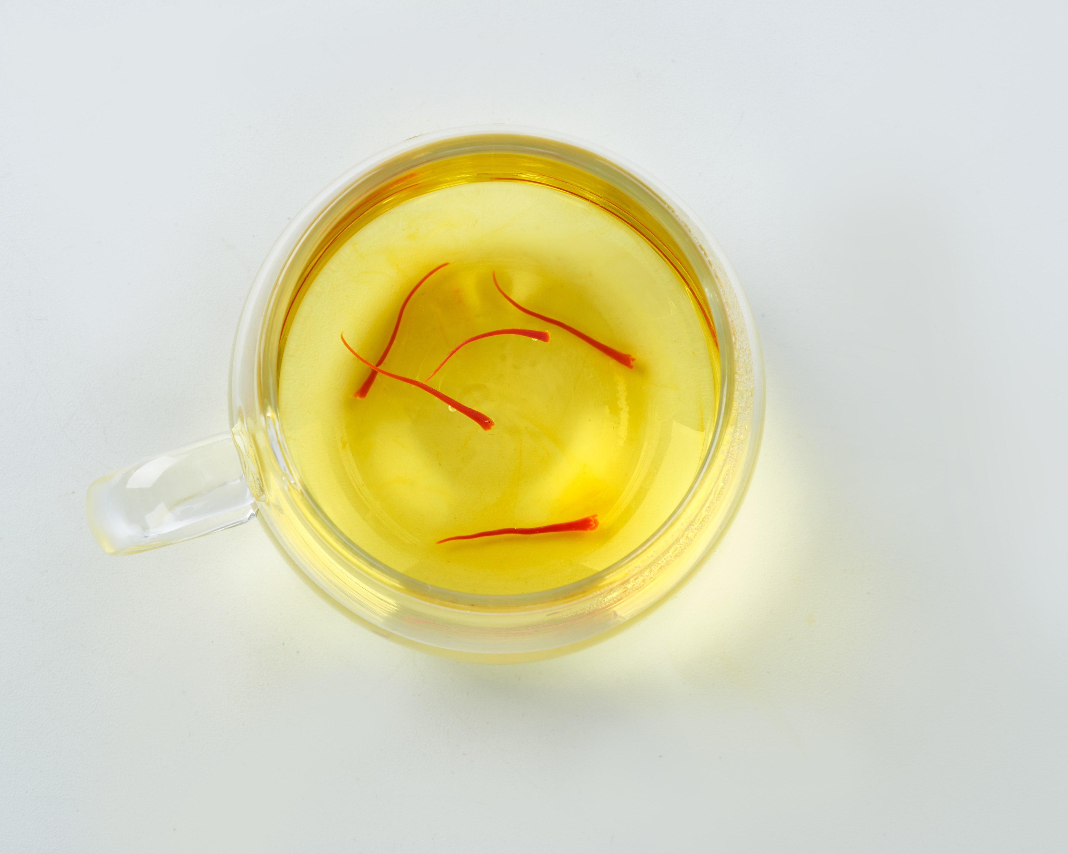 图片说明:透明玻璃杯中正在冲泡的金丝皇菊与藏红花,茶水呈淡黄色,藏红花丝清晰可见,背景柔和自然 藏红花与金丝皇菊冲泡过程图