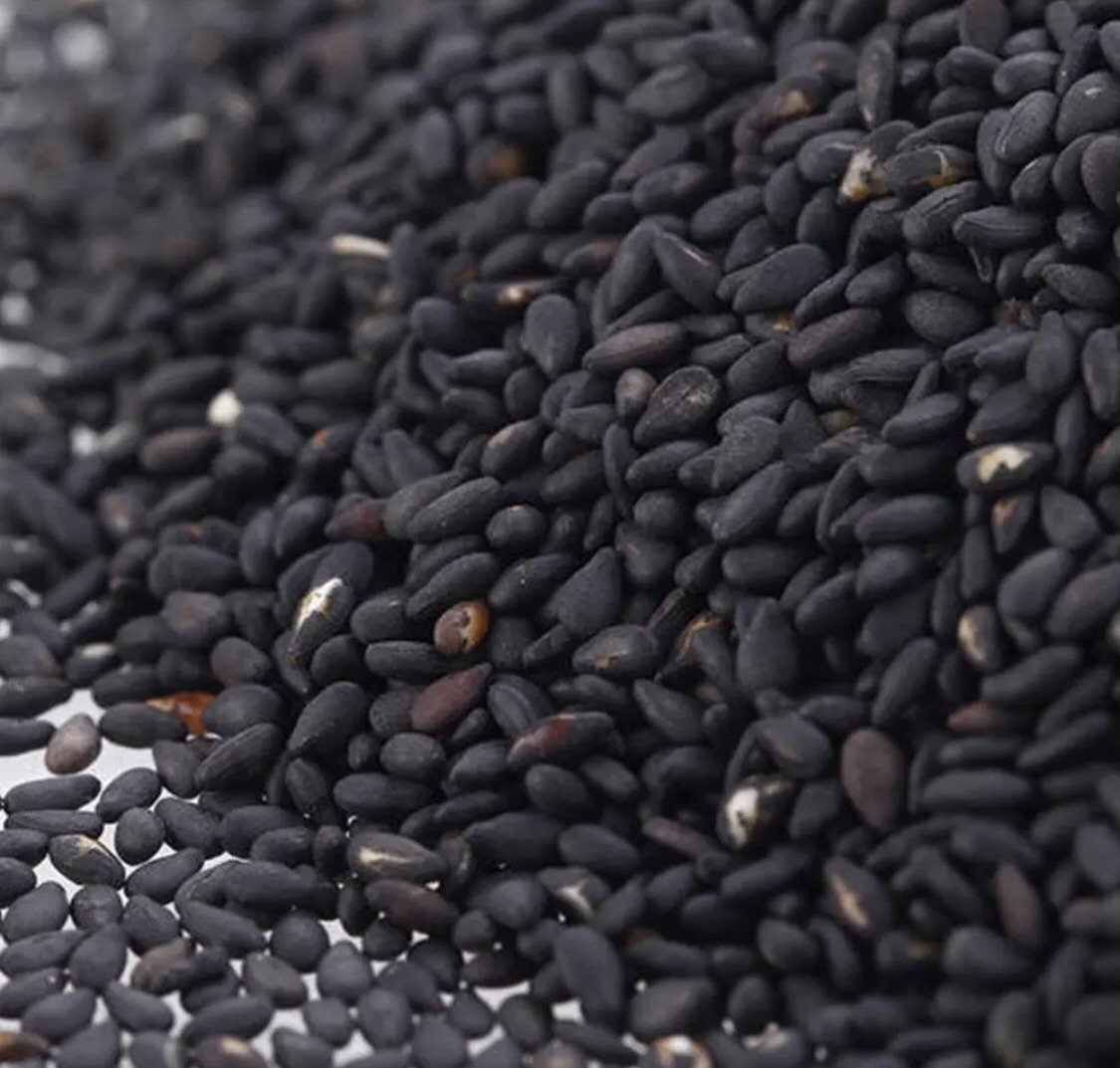 高清特写镜头下的黑芝麻颗粒,表面光滑有光泽,呈深黑色卵圆形,散落在木质托盘上,背景虚化的中药柜暗示其传统药用价值 黑芝麻中药材特写