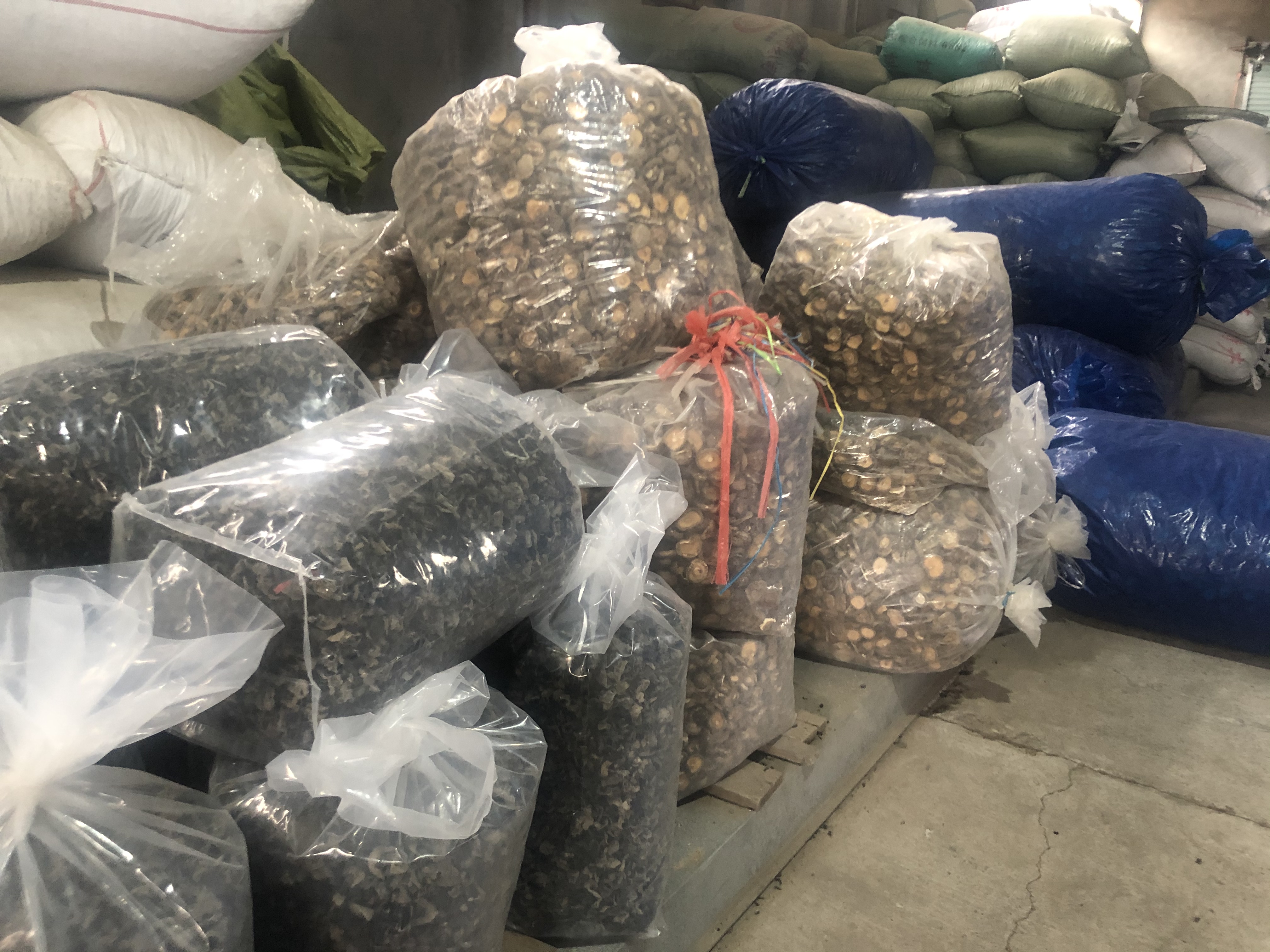 一个传统农贸市场摊位,木质货架上整齐排列多个麻布袋,分别标注‘一级花菇’‘特厚干香菇’‘普通薄菇’,摊主正在称重,顾客围观选购,背景可见其他农产品 干香菇市场摊位实景