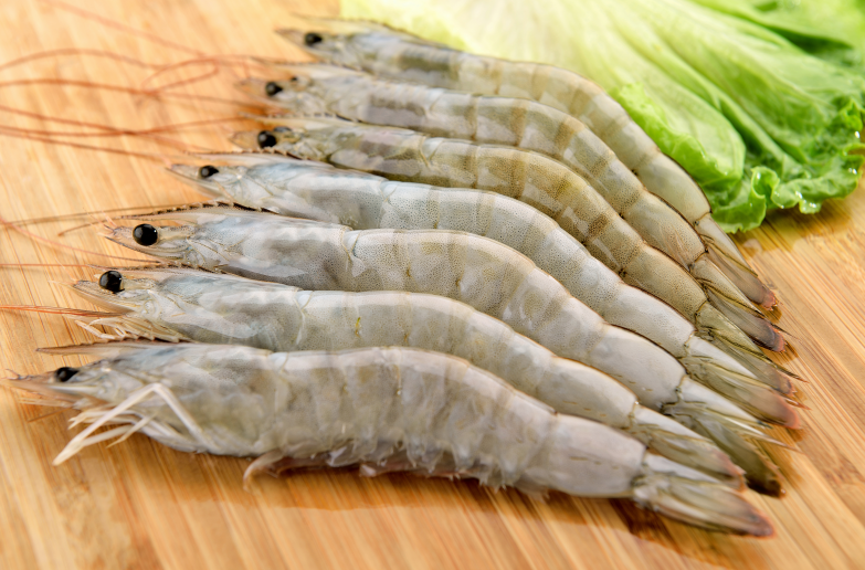 一位厨师戴手套在砧板上使用牙签挑出对虾背部的虾线,旁边摆放已完成去线的洁白虾仁,背景有清水碗和不锈钢夹子 厨房操作场景