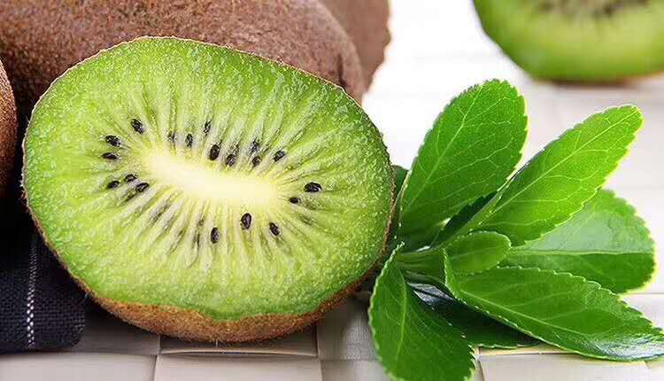 一盒完整的绿色表皮徐香猕猴桃摆放在木质桌面上,旁边是一颗被横向切开的果实,露出翠绿果肉与整齐排列的黑色种子,背景有水珠点缀,展现新鲜质感 徐香猕猴桃礼盒装与切开的鲜果特写