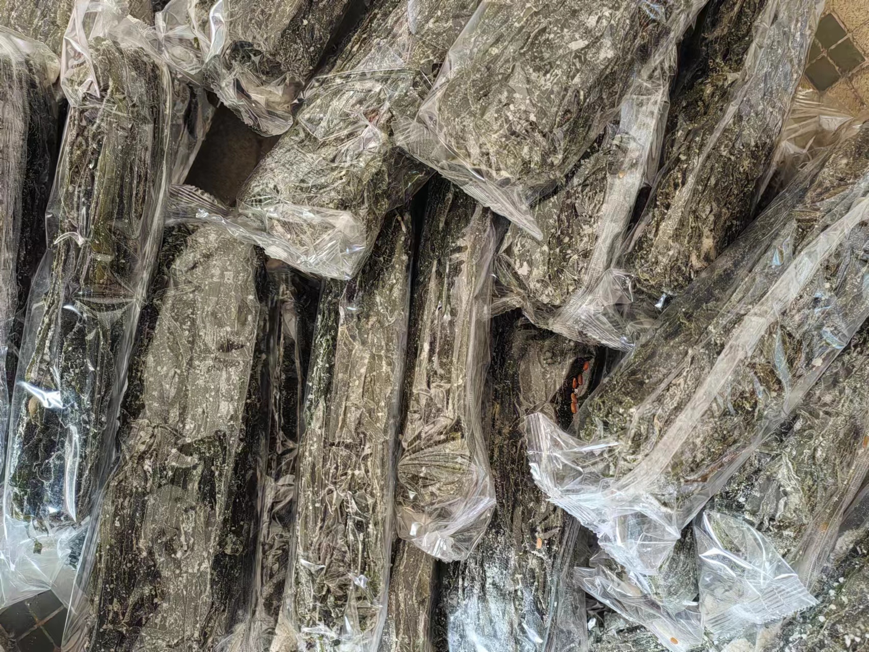 一张高清照片展示摊位上堆放的干海带,部分叶片表面可见明显的白色絮状覆盖物,光线照射下呈现半透明质感,旁边配有标注‘天然孢子囊’的提示牌 市场中售卖的干海带特写
