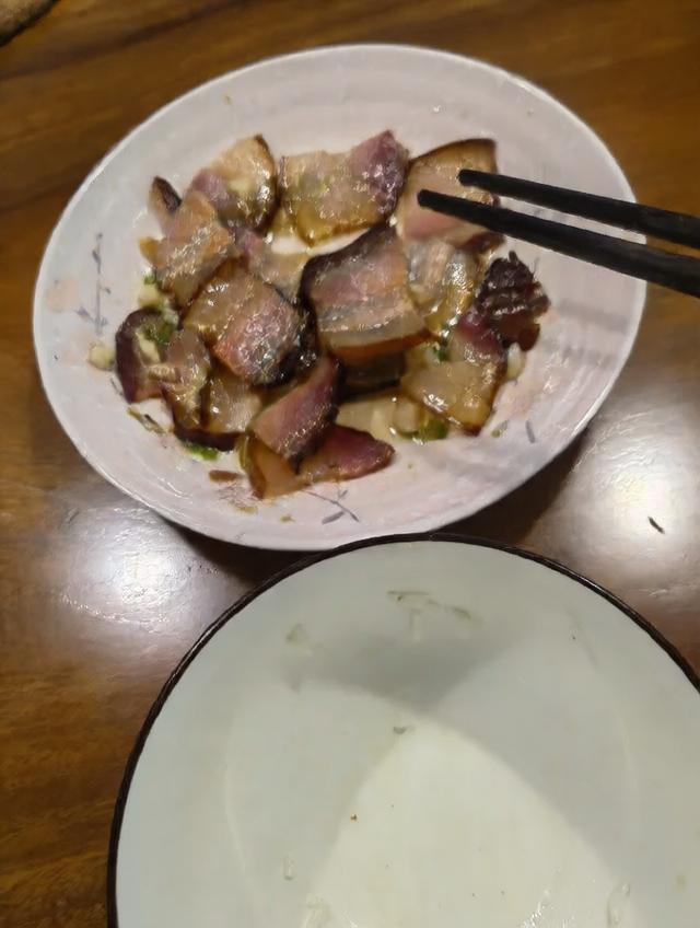 一盘热气腾腾的家常菜——白辣椒炒腊肉,深色腊肉片与米白色的辣椒段混合翻炒,油光微亮,配以蒜苗点缀,盛放在粗瓷碗中,背景为农家木桌和竹筷,体现地道乡土风味 白辣椒家常菜肴