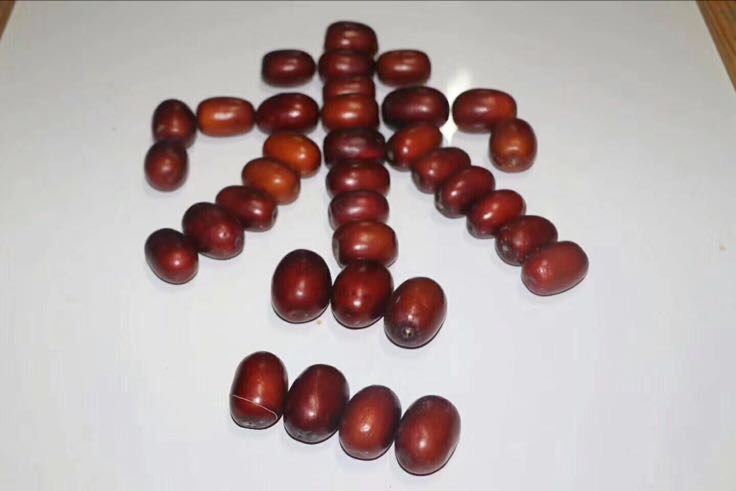 透明玻璃罐中盛满金红色的脆枣，旁边摆放一碟散装脆枣和一杯绿茶，桌面铺着木质纹理布艺