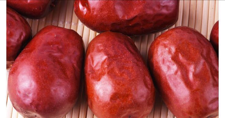 一颗饱满红润的骏枣特写镜头,表皮光滑有光泽,果肉厚实,呈现出自然成熟的深红色,背景为干燥整洁的木质托盘,突显其高品质特征 骏枣特写