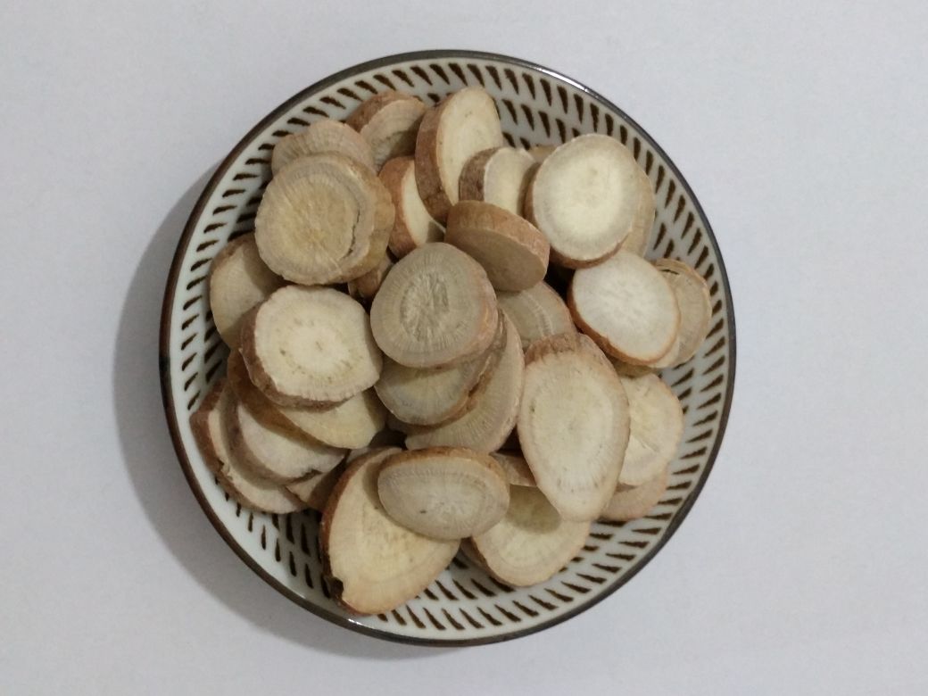 高清微距摄影:左侧为甘肃岷县当归饮片(断面黄白色,油点明显,香气浓郁);中部为浙江杭白芍饮片(类圆形薄片,表面类白色,中心淡棕色形成明显筋脉纹);右侧为湖南怀化野生葛根切片(浅黄棕色,纤维性强,断面可见放射状纹理与同心环纹。三者按比例1:1:1置于青瓷盘中,背景为竹制中药斗柜,体现道地性与食药同源属性 当归白芍葛根三味药材实物对比图