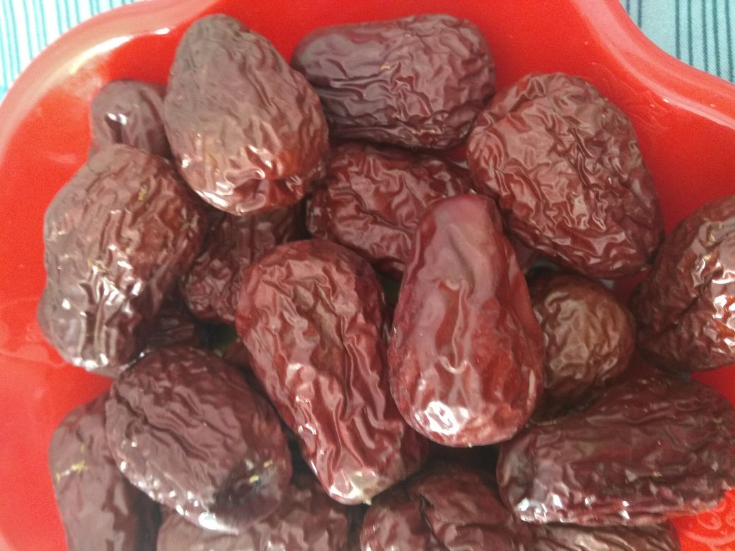 一颗饱满红润的新疆和田大枣,表皮光滑有光泽,果肉厚实,呈现自然深红色,背景为浅色木质托盘,旁边配有剖开的大枣展示内部果核与果肉结构 和田大枣特写