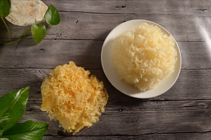 新鲜银耳一朵呈淡黄色、质地柔软,旁边摆放两个翠绿带柄的新鲜香梨,背景为木质砧板与白色瓷碗,光线柔和自然,突出食材原生态质感 银耳与香梨食材摆盘图