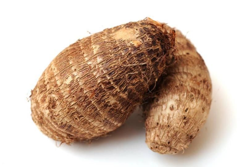 一位家庭主妇正在厨房用刀具削去香芋的外皮,香芋表面湿润,有白色汁液渗出,背景为木质案板和水槽,光线自然明亮 香芋去皮过程特写