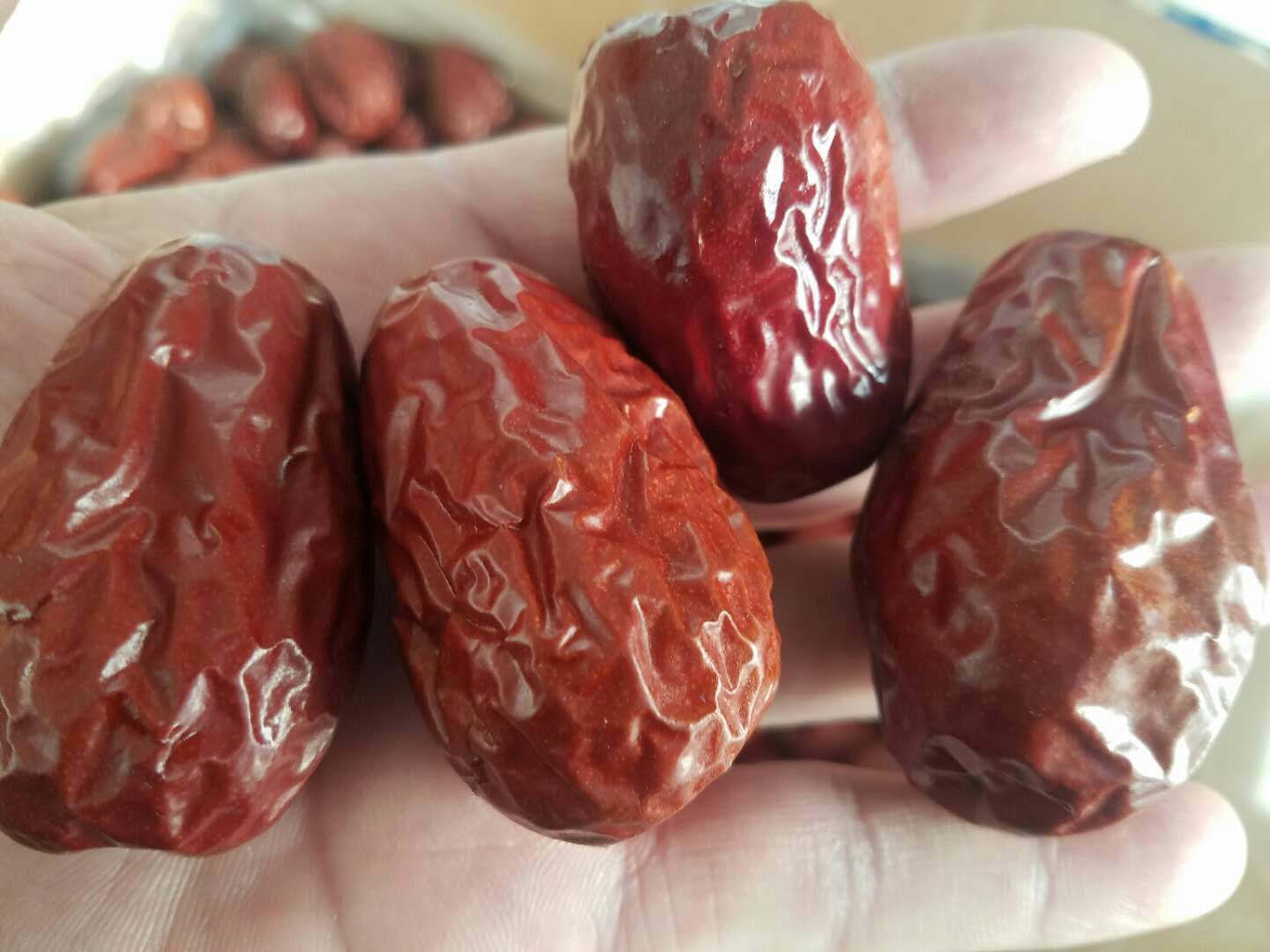 一颗饱满红润的干红枣,表面有自然褶皱,一侧可见明显的果核凸起,背景为木质砧板,突出其天然农产品属性 红枣特写