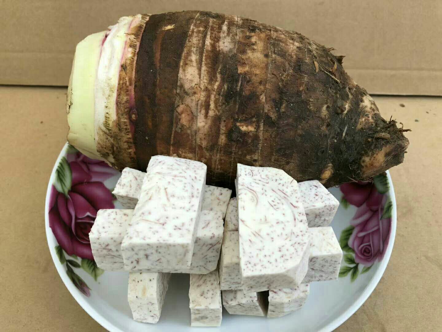 新鲜荔浦芋头被去皮后切成均匀的滚刀块,部分已放入沸水中焯烫,锅边有轻微蒸汽升起,旁边摆放着生姜片、大蒜瓣和香料 荔浦芋头切块与焯水过程