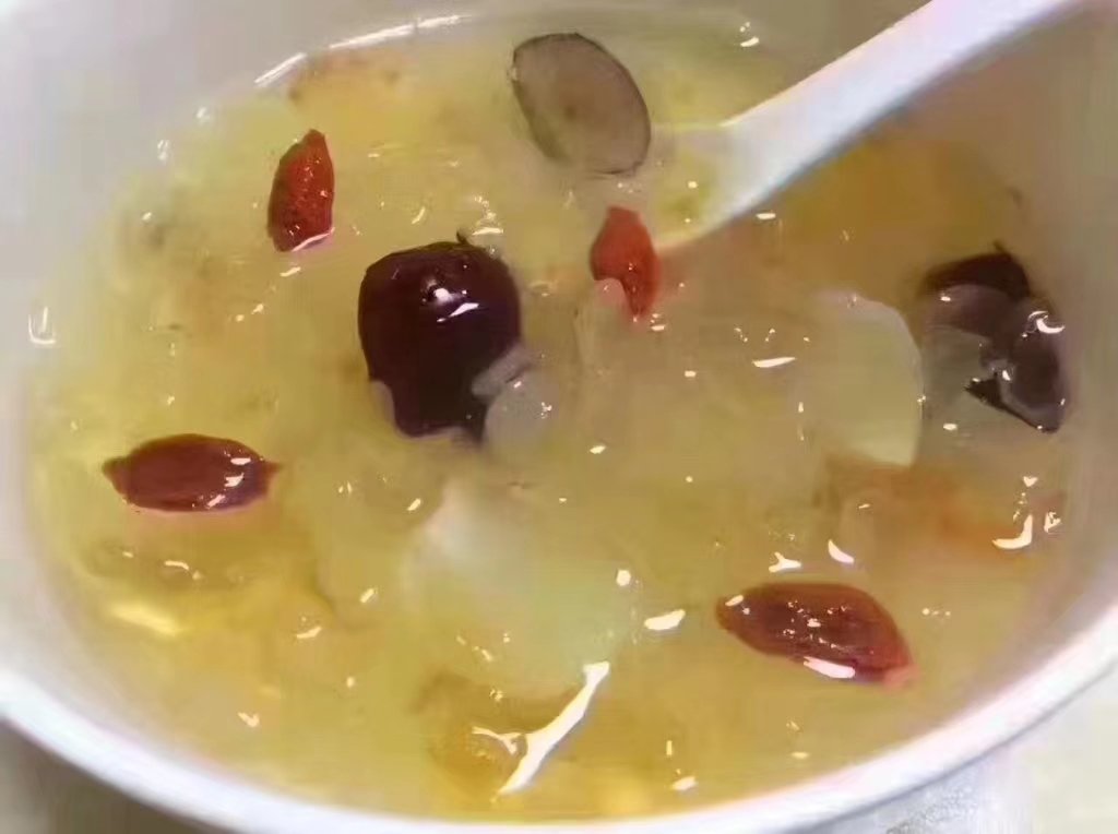 白色瓷碗中盛放炖煮90分钟后的古田丑耳甜品,银耳完全出胶,汤体浓稠呈琥珀色,表面漂浮枸杞与红枣,勺子插入可见拉丝状胶质。背景虚化,突出食物质感与光泽 古田丑耳炖煮成品特写图