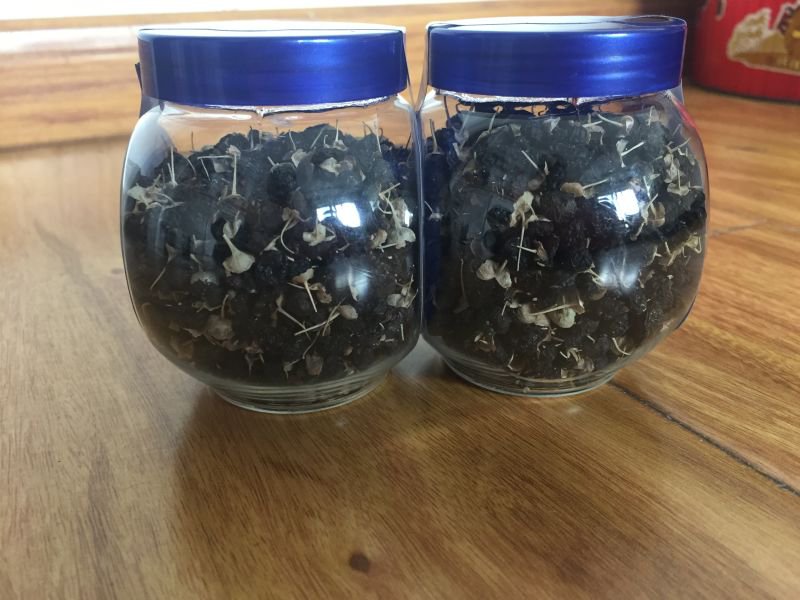 一个透明玻璃罐装黑枸杞放置在阴凉柜中,标签注明‘密封避光保存’;旁边是一个敞口碗暴露在阳光下的黑枸杞,部分已发黏变色,形成鲜明对比 黑枸杞储存对比示意图