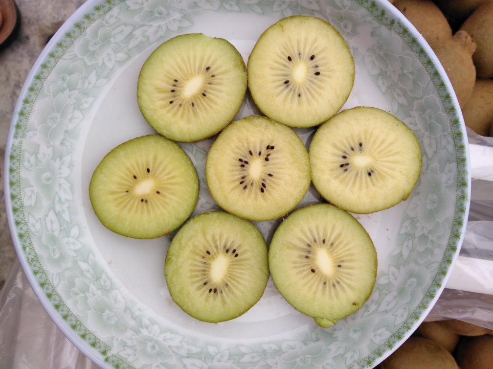 一位孕妇坐在餐桌前,正在切开一颗新鲜的黄心猕猴桃,桌上还有其他水果和早餐食物 孕妇吃水果场景