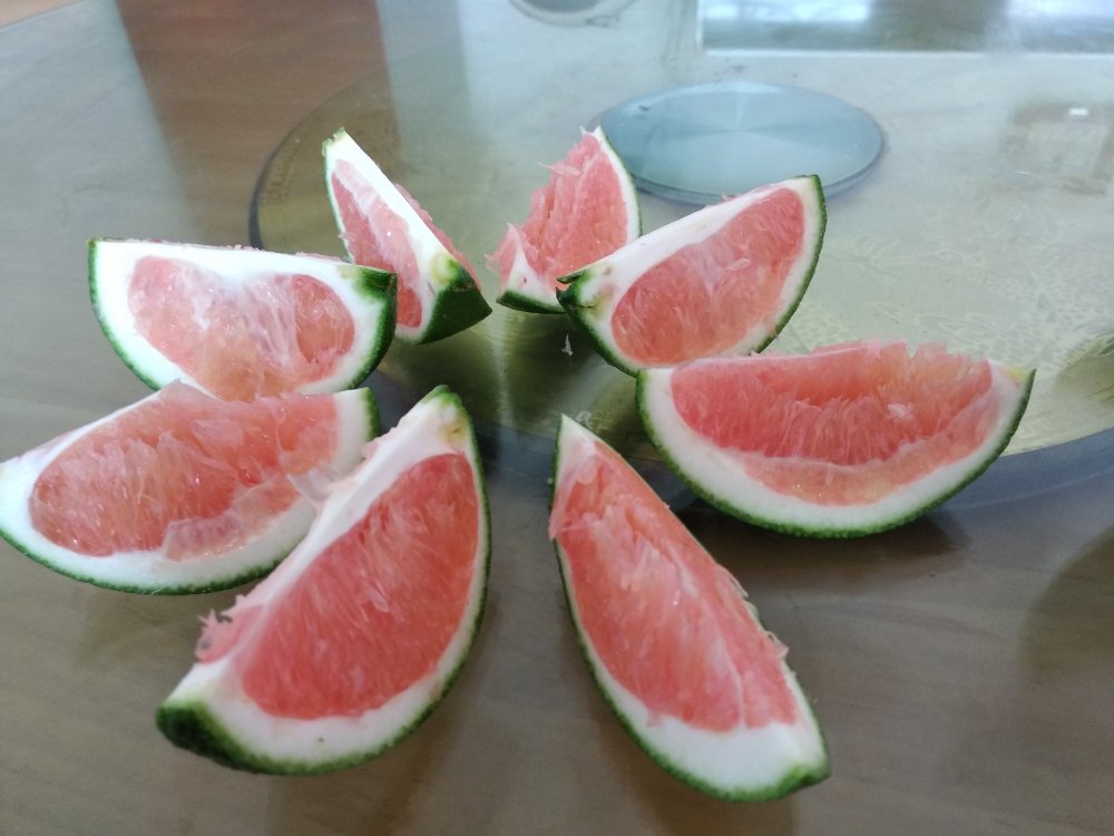 现代厨房餐桌上摆放切开的赣南脐橙,果肉饱满多汁,旁边配有玻璃水杯和儿童餐盘,一家三口正在愉快分享,体现健康饮食生活方式 家庭享用赣南脐橙场景图