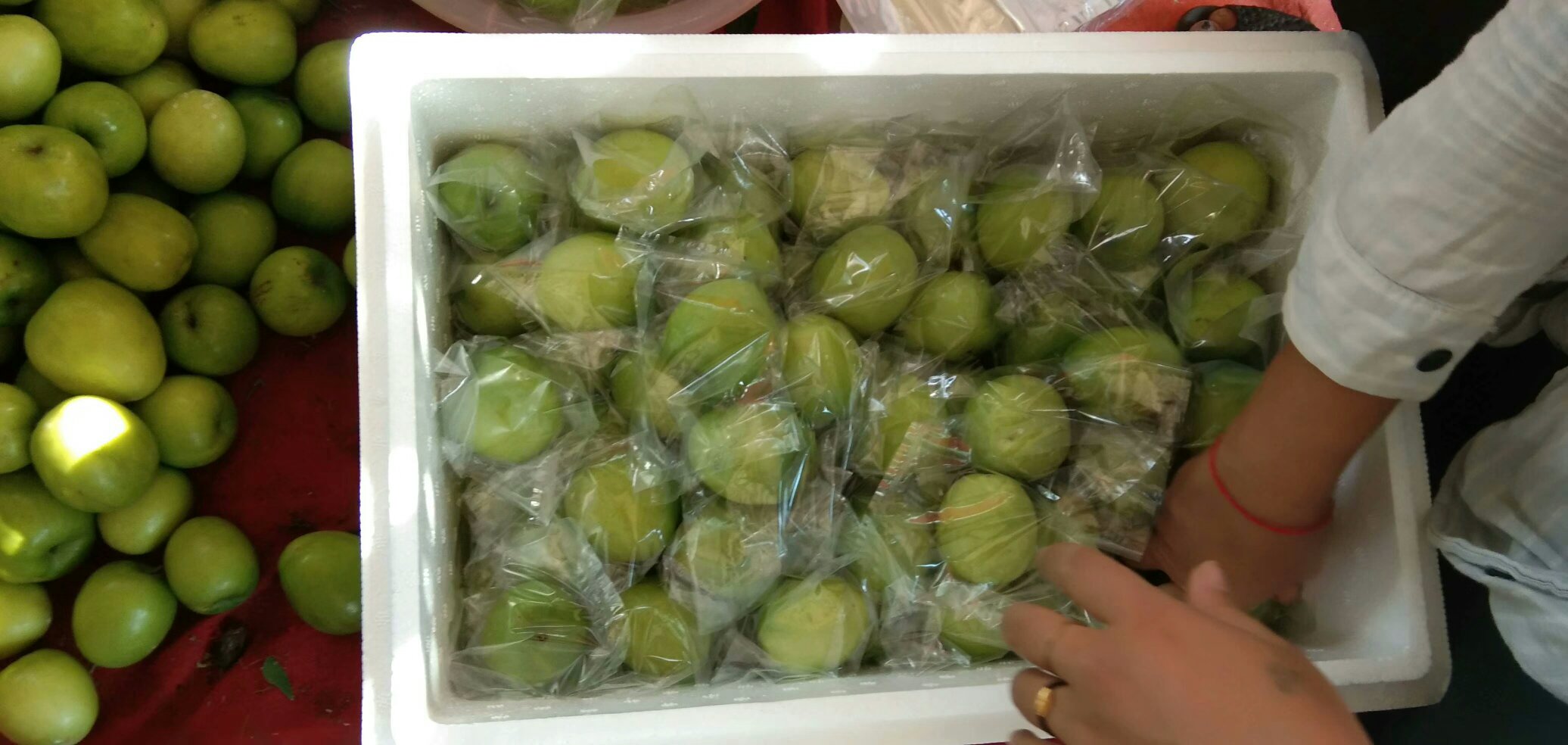 一箱精美的青枣礼盒摆放在木质桌面上,旁边是散装的新鲜青枣,背景为现代化水果批发市场,工作人员正在进行分拣和打包作业,体现青枣的商品化流程 青枣包装与销售场景