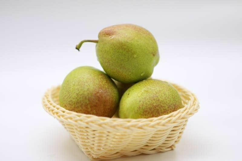 一筐新鲜采摘的绿色香梨放置在木质托盘上,背景为果园环境,部分香梨表面有自然光泽,展示其原始新鲜状态 香梨在自然环境下的存放状态