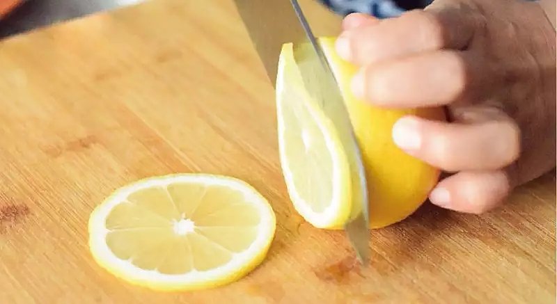 一名厨师正在厨房操作台上用盐和小苏打搓洗一个新鲜的安岳柠檬,旁边摆放着切好的柠檬薄片和半个已榨汁的柠檬,背景为木质料理台面,光线自然明亮 安岳柠檬清洗与切片过程