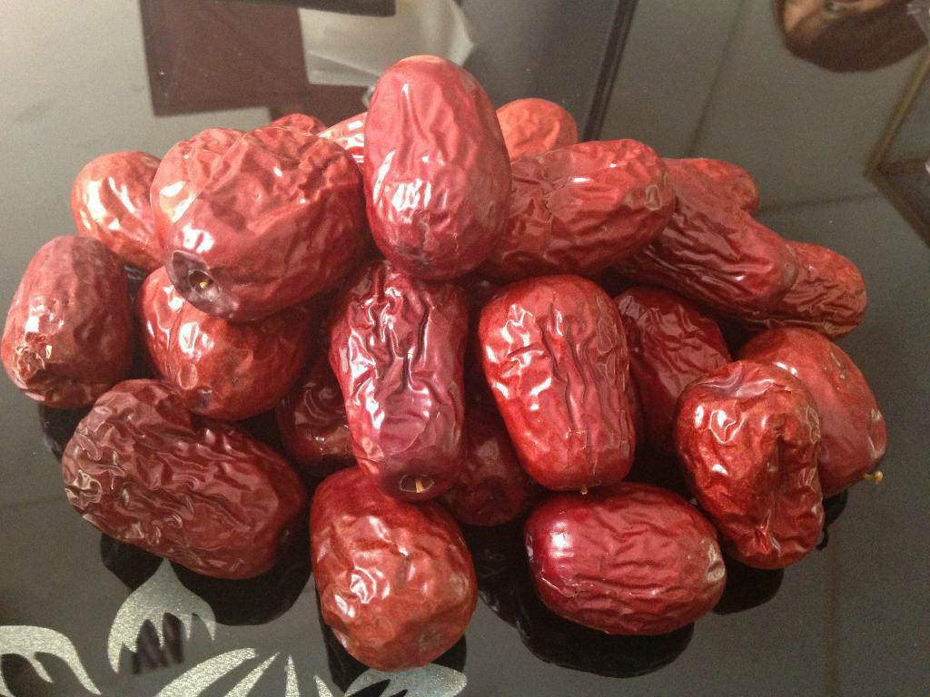 航拍视角下的若羌县规模化灰枣种植基地,展现典型暖温带大陆性干旱气候下的枣树生长状态,果实着色均匀、糖分积累充分,印证地理标志产品独特风土条件 若羌灰枣产地实景:塔里木盆地东缘戈壁绿洲,成片枣园枝头挂满深红色果实,阳光下果面泛琥珀色光泽,远处可见阿尔金山脉