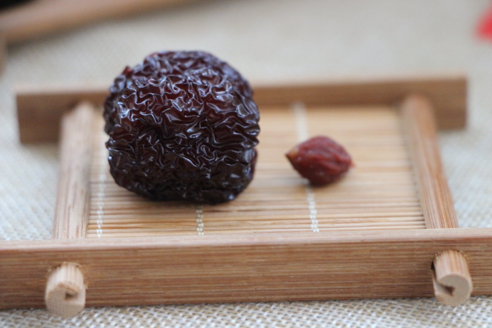 一张高清微距摄影图片,左侧为三颗标准长枣(长约4-5厘米),右侧为五颗微枣(长约2-2.5厘米),两者并列摆放于木质托盘上,背景为柔和自然光下的厨房环境,突出尺寸差异与表皮光泽对比 微枣特写对比图