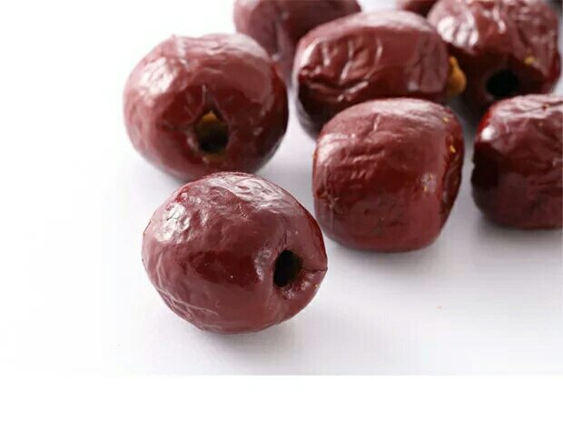 孩子开心地用手抓起一把脆枣放入嘴里，家长在一旁微笑注视，背景为家庭客厅环境，桌上放有果盘和饮料