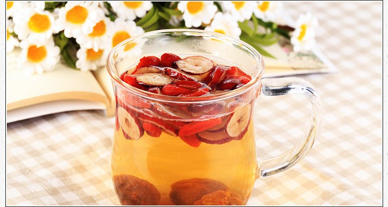 一位身穿浅色家居服的孕妇坐在阳光充足的客厅沙发上,手中拿着一小碗装有干红枣片的玻璃碗,面带微笑准备食用,旁边放着一杯温水和一本孕期营养书籍,环境温馨舒适 孕妇食用红枣场景